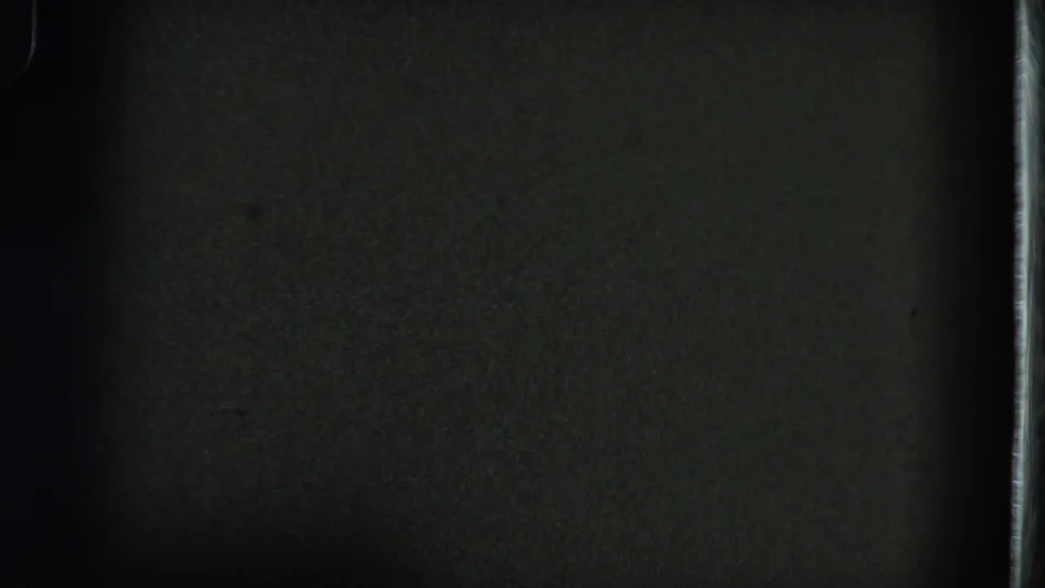 This dim 8mm frame shows mostly dark wall and film texture, with the subject not clearly visible in the sampled still.