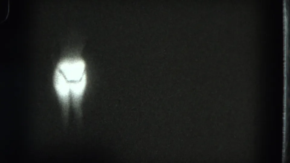 1975 San Francisco 8mm frame with a small glowing human-like lower-body silhouette in darkness and heavy film grain.