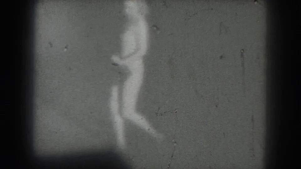 The performer is more visible as a soft white silhouette moving through the lower-left frame in 1975 8mm footage.