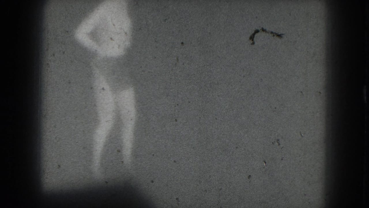 1975 San Francisco 8mm frame showing a distant silhouetted performer with raised arms, softened by grain, dust, and low contrast.