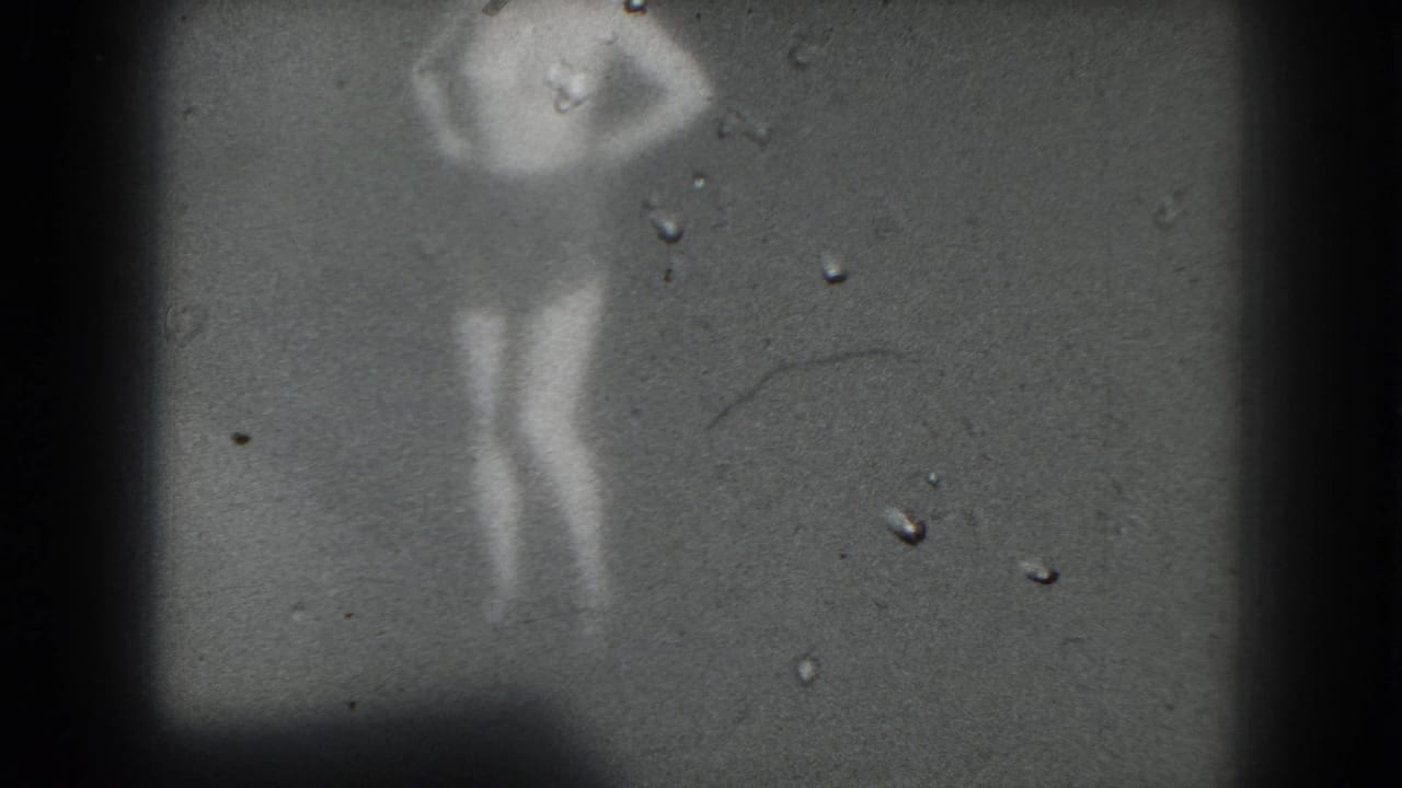 1975 San Francisco 8mm frame with a blurred stage performer, one arm bent near the head, surrounded by dust marks and dark borders.