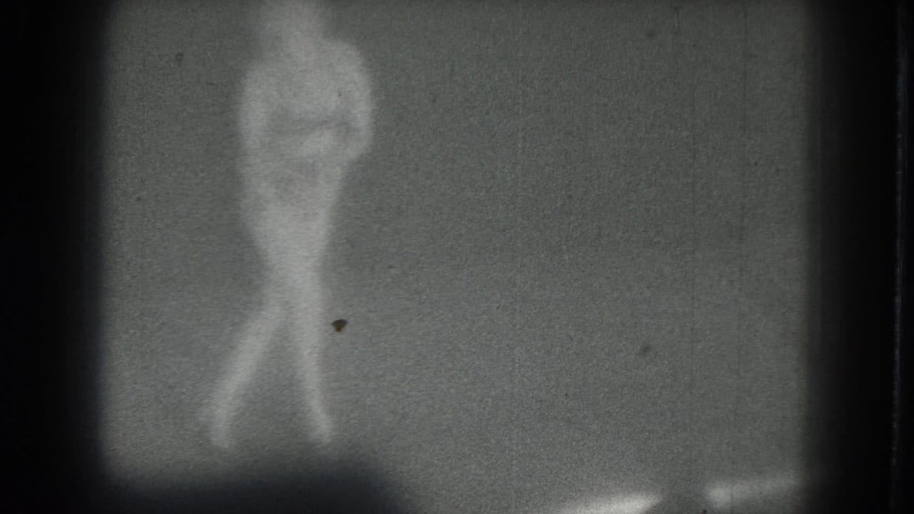 A low-light 8mm frame shows the dancer mid-movement, with her body softened by blur and grain.