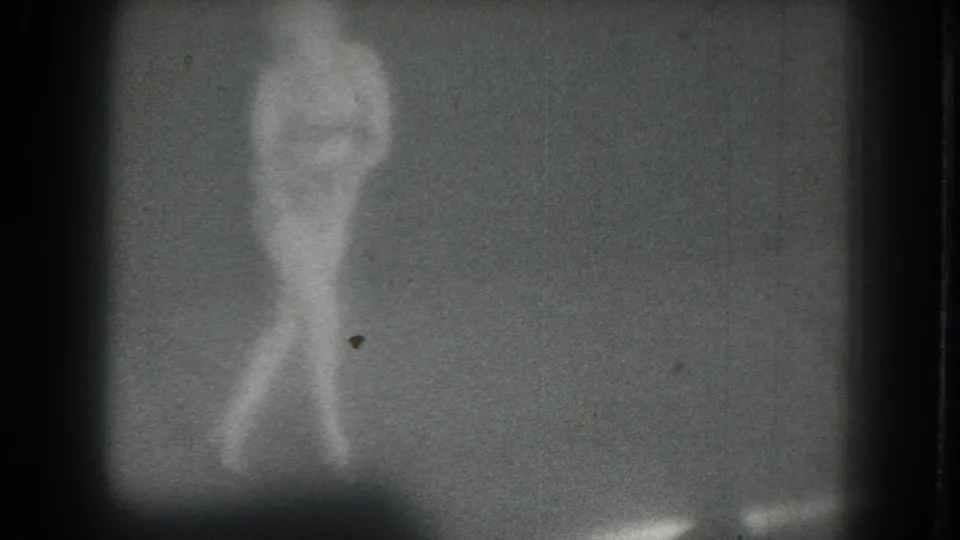 A low-light 8mm frame shows the dancer mid-movement, with her body softened by blur and grain.