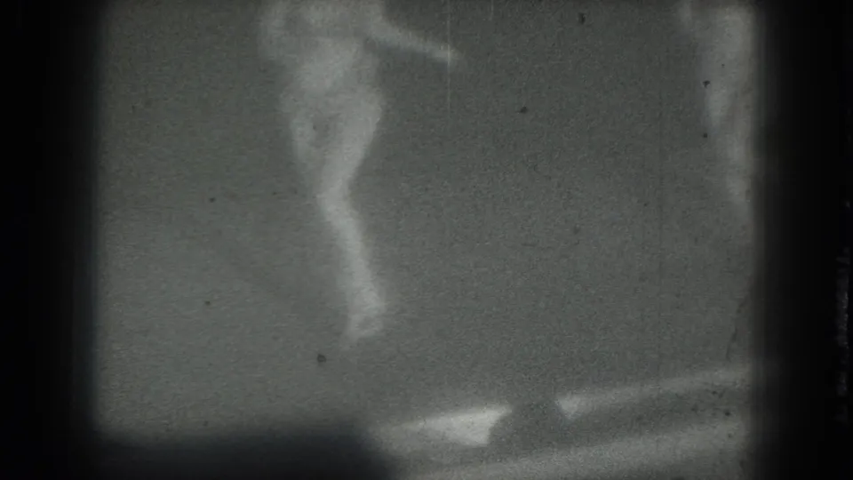 The 8mm frame catches the dancer partly cropped, with legs and stage floor visible through heavy grain.