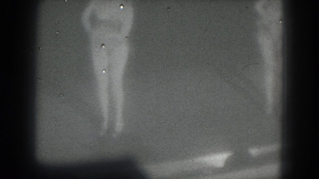 1975 San Francisco 8mm frame with a barely visible stage figure obscured by darkness, grain, and vertical shadows.