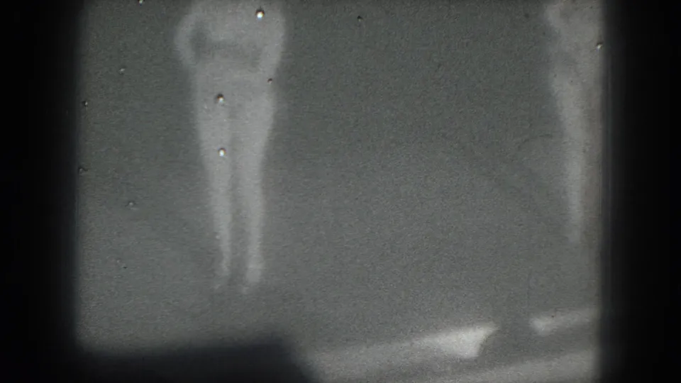 1975 San Francisco 8mm frame with a barely visible stage figure obscured by darkness, grain, and vertical shadows.