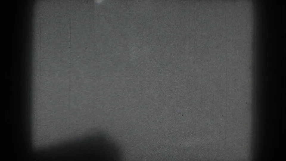1975 San Francisco 8mm frame reduced to abstract shadows, grain, and a dark lower shape, with no clear figure visible.
