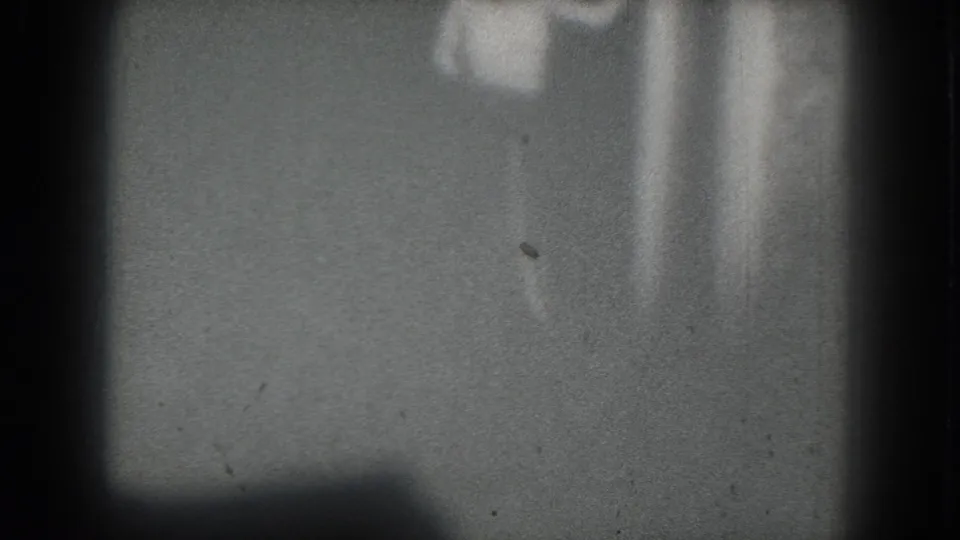 1975 San Francisco 8mm frame with a barely discernible performer-like form at right amid shadows, scratches, and soft exposure.