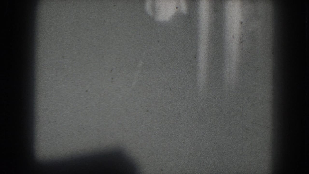 1975 San Francisco 8mm frame with an indistinct topless stage performer barely visible against a gray backdrop.