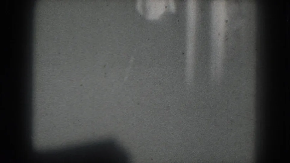1975 San Francisco 8mm frame with an indistinct topless stage performer barely visible against a gray backdrop.
