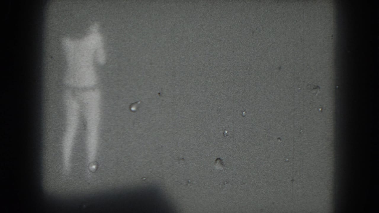 Soft, grainy frame of a woman dancing on a dim stage against a dark backdrop.