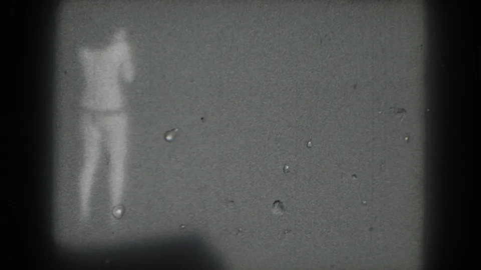 1975 San Francisco 8mm frame showing a distant woman in light clothing dancing on a dark, softly focused stage.