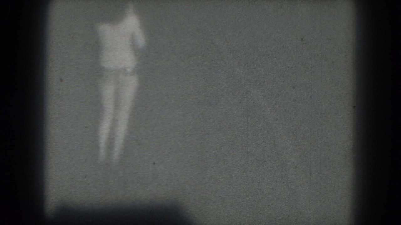 A grainy 1975 San Francisco 8mm frame shows the performer blurred by motion and distance on a dim stage.