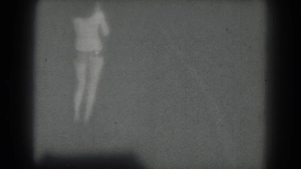 A grainy 1975 San Francisco 8mm frame shows the performer blurred by motion and distance on a dim stage.