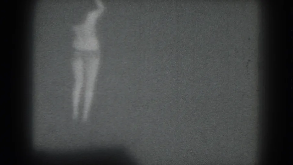 The home-movie frame shows a distant woman dancing at left, with strong grain and dark vignetting around the 8mm image.