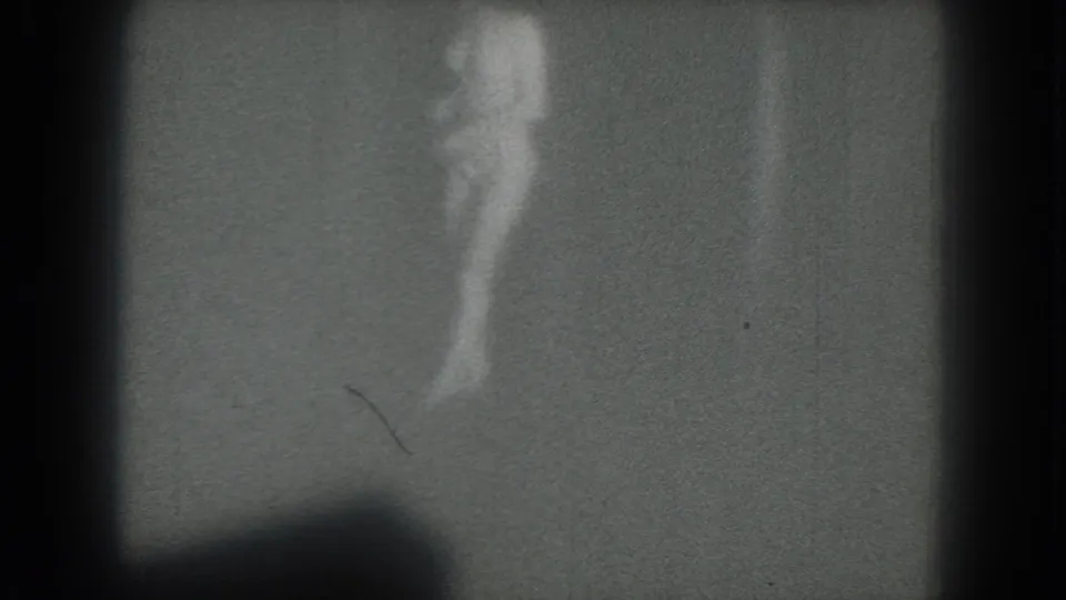 Grainy side-view frame from the 1975 San Francisco clip, showing the woman mid-turn against a sparse background.