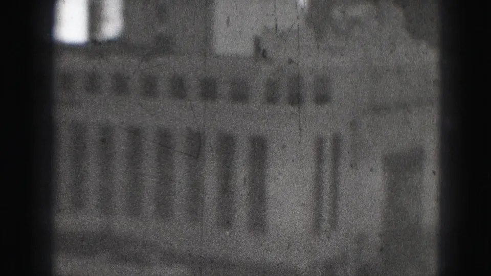 Grainy 1975 Harrisburg home-movie frame showing a blurred office facade through a dark-edged window or lens view.