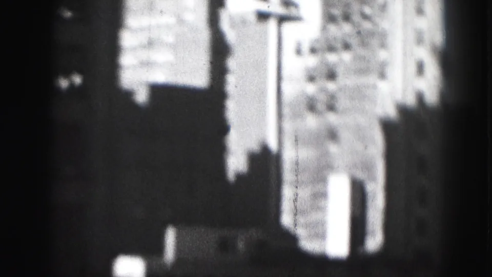 1975 Harrisburg high-rise buildings appear in soft focus through a dark window frame on black-and-white 8mm film.