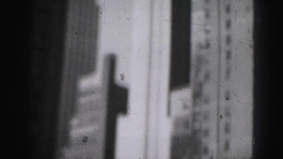 Black-and-white 8mm frame showing Harrisburg high-rise walls and a streetlamp form passing across the foreground.