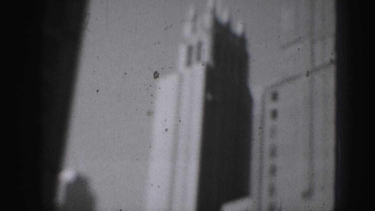 1975 Harrisburg home-movie frame showing a soft, grainy view of a high-rise edge and stepped crown against bright sky.