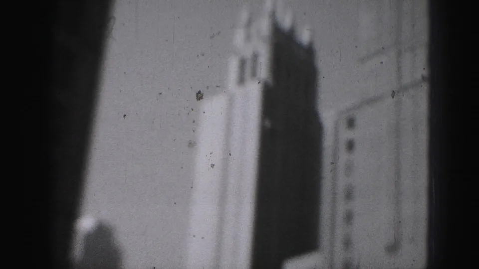 1975 Harrisburg home-movie frame showing a soft, grainy view of a high-rise edge and stepped crown against bright sky.