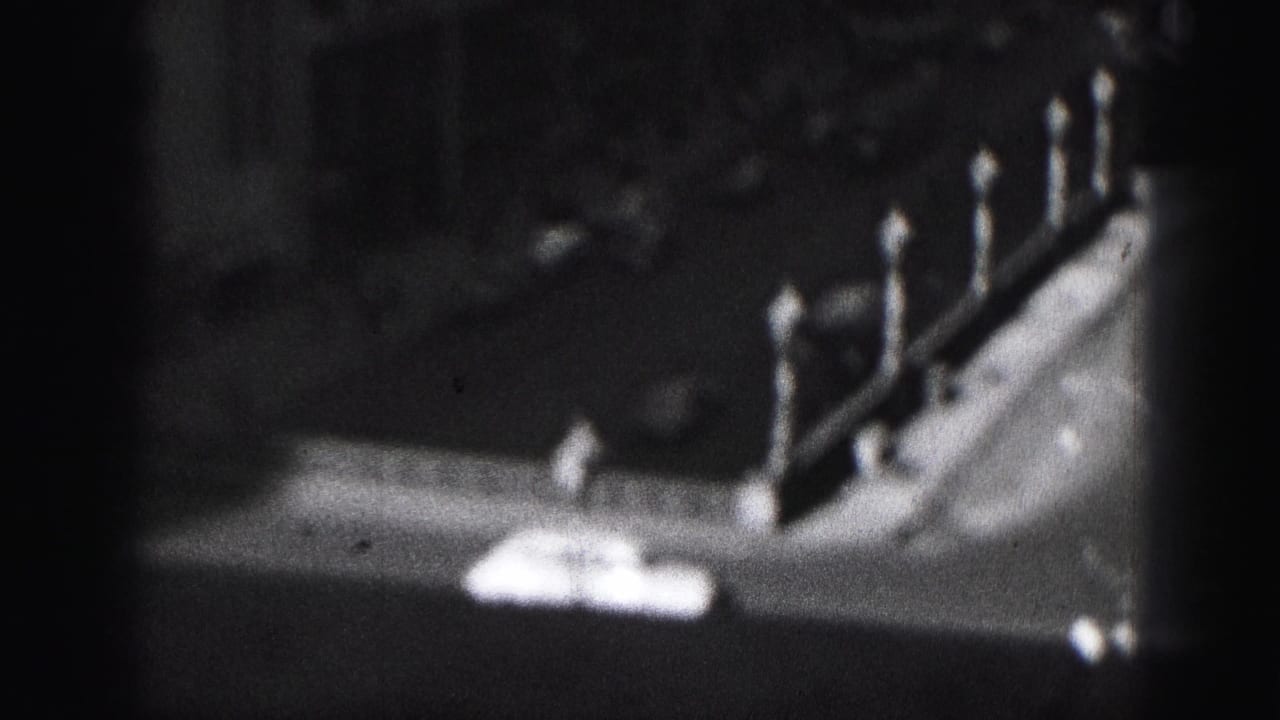 Grainy 1975 Harrisburg frame with a shadowed rooftop or parapet edge, pointed posts, and indistinct downtown buildings.