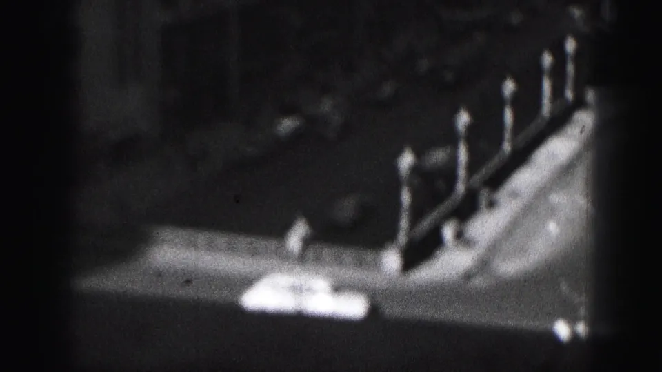 Grainy 1975 Harrisburg frame with a shadowed rooftop or parapet edge, pointed posts, and indistinct downtown buildings.