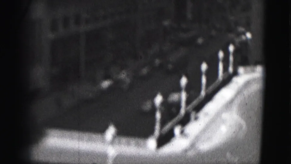 1975 Harrisburg home-movie frame showing a parapet-like edge with pointed posts, soft focus, and dark urban background.