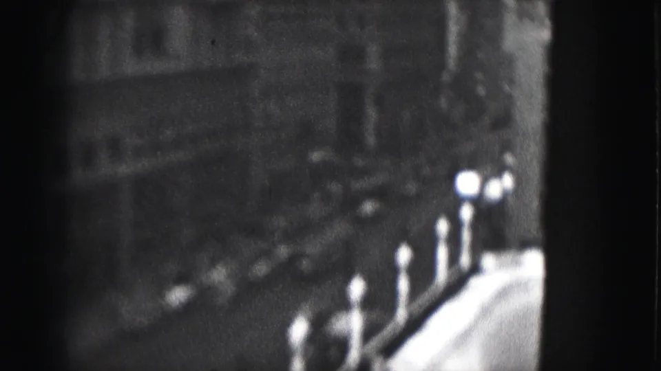 Final 1975 Harrisburg frame with dark masonry buildings, a parapet line, bright highlights, and heavy 8mm vignetting.