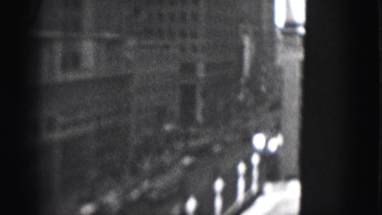1975 Harrisburg 8mm frame showing a tall urban building facade in soft focus with dark framing and bright window highlights.