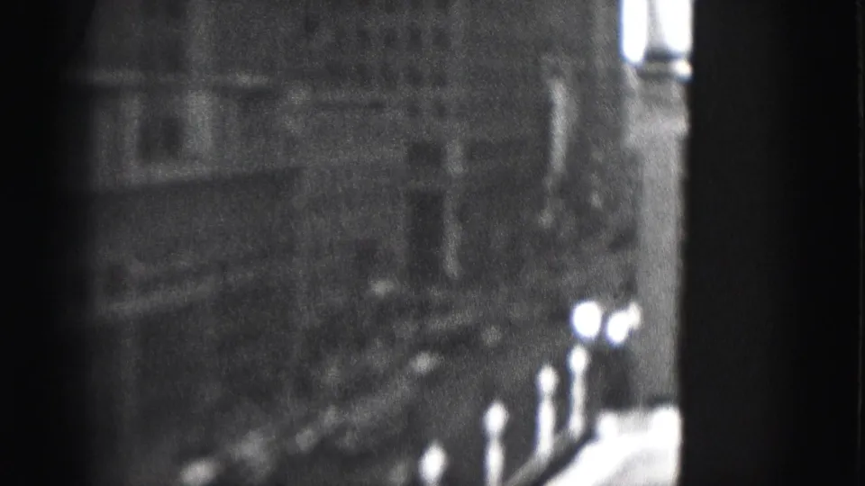 1975 Harrisburg 8mm frame showing a tall urban building facade in soft focus with dark framing and bright window highlights.