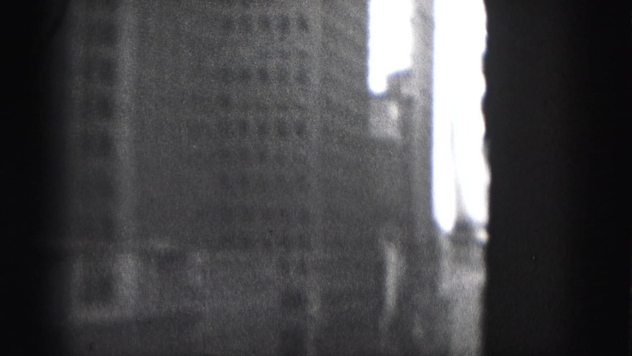 Black-and-white 8mm frame from Harrisburg showing a shadowed building face and a bright sky gap along the right edge.