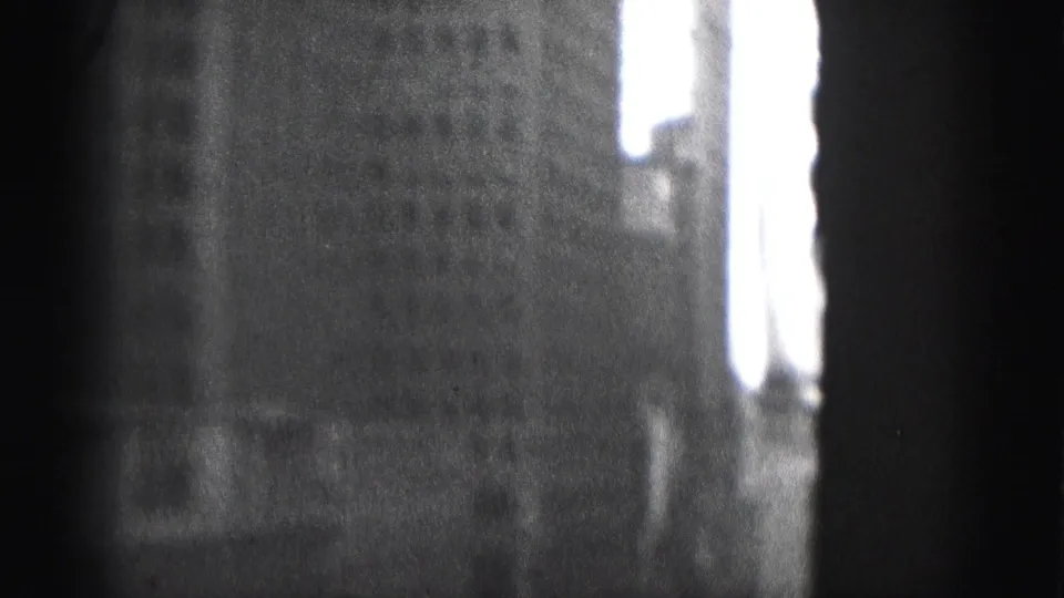 Black-and-white 8mm frame from Harrisburg showing a shadowed building face and a bright sky gap along the right edge.