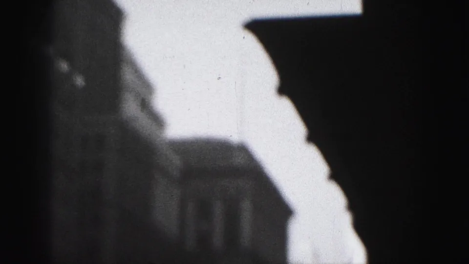 Black-and-white Harrisburg home-movie frame with a bright angular building edge and shadowed facade details.