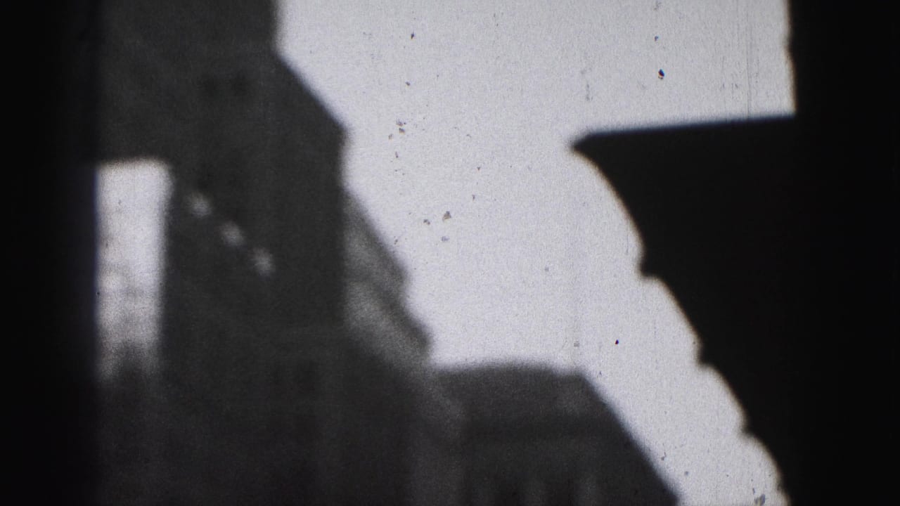 1975 Harrisburg home-movie frame with a dark window edge and soft silhouettes of tall downtown buildings.