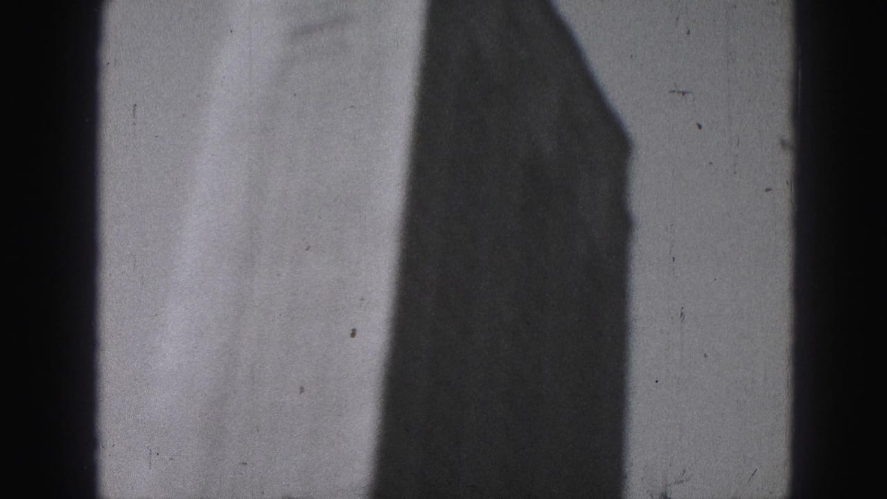 1975 Harrisburg home-movie frame showing a soft, dark tower silhouette and film border against a hazy pale sky.