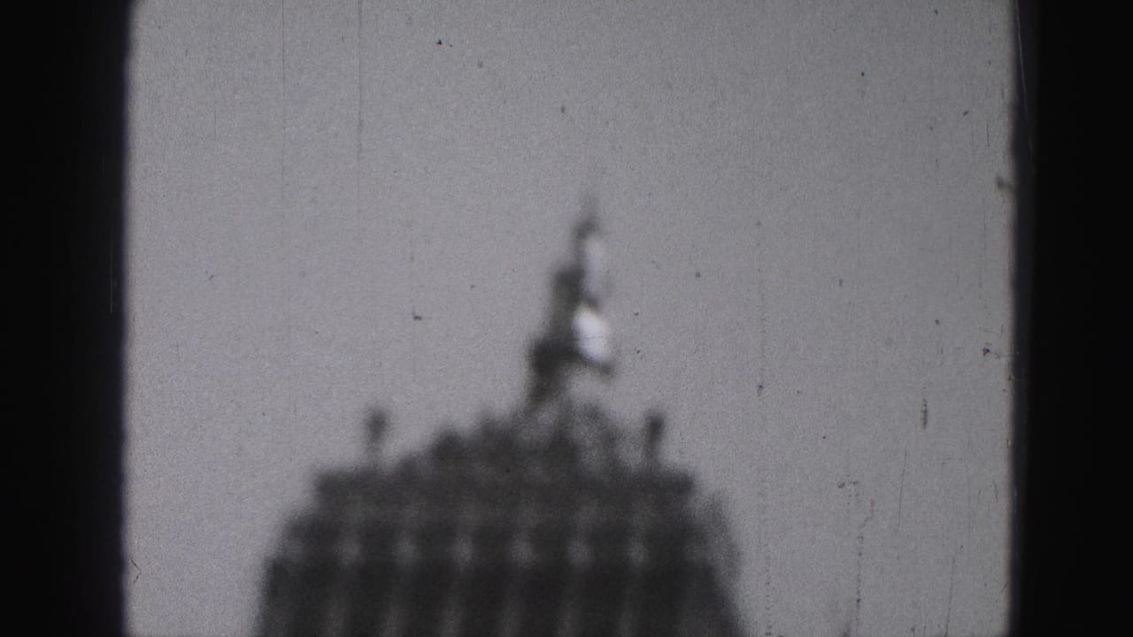 1975 Harrisburg 8mm frame with a blurred tower crown and small spire partly framed by a dark vertical foreground shape.
