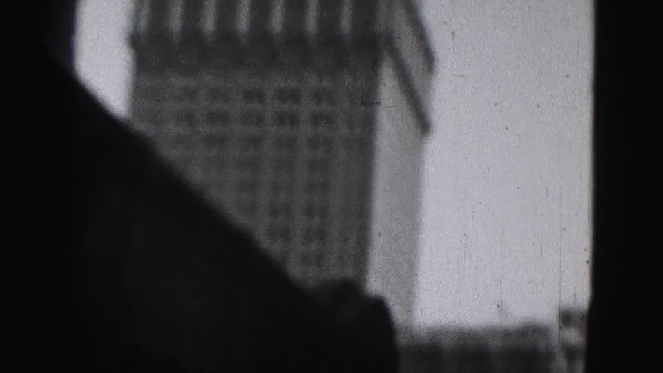 1975 Harrisburg 8mm frame with a tower top and spire partly blocked by a dark foreground silhouette and visible film wear.