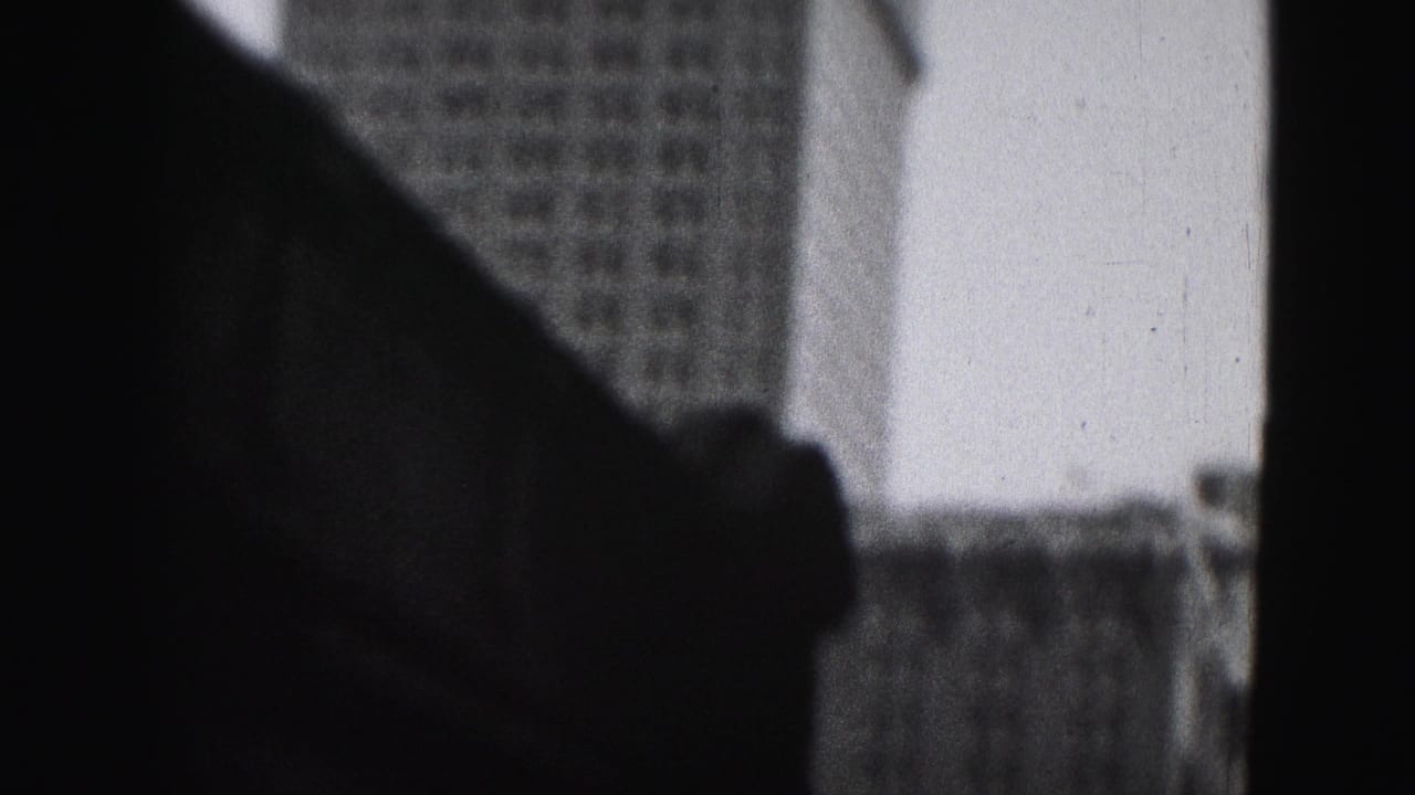 A 1975 Harrisburg home-movie frame shows dark window or vehicle framing with office buildings partly visible beyond it.