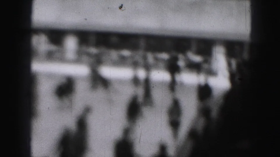 Grainy 1975 Harrisburg frame with scattered skaters on an outdoor ice rink, heavily softened by focus.