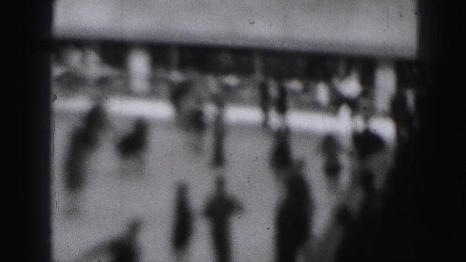 Soft black-and-white 8mm frame of a crowded Harrisburg rink in 1975, with indistinct skaters and spectators near the boards.