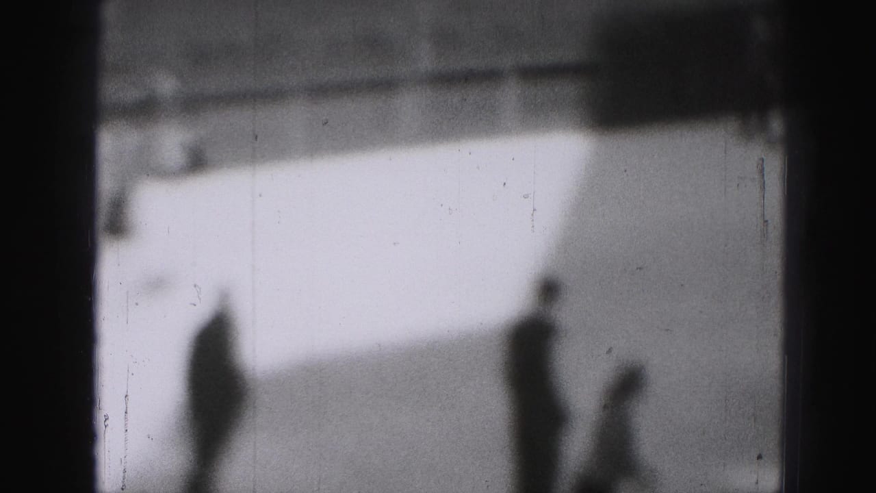 Soft 1975 8mm frame from Harrisburg showing silhouetted skaters spread across an outdoor ice rink.