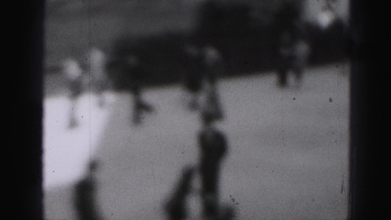 Several blurred skaters cross an outdoor rink with indistinct background shapes.