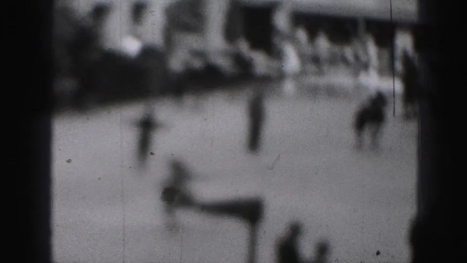 Grainy 1975 home-movie frame showing distant skaters on an outdoor rink in Harrisburg, Pennsylvania.
