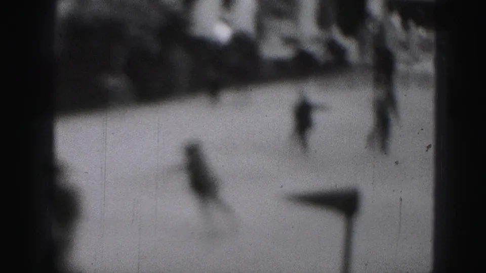 Soft black-and-white 8mm frame with a foreground skater and other distant figures on a Harrisburg outdoor rink.