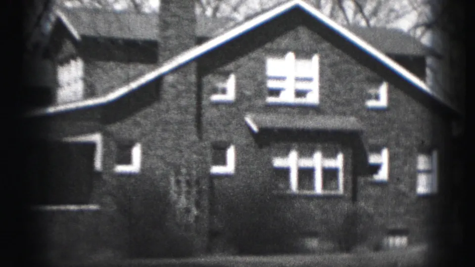 Late frame of the 1975 Harrisburg 8mm clip showing the brick house facade, bright windows, chimney, and dark gate edge.