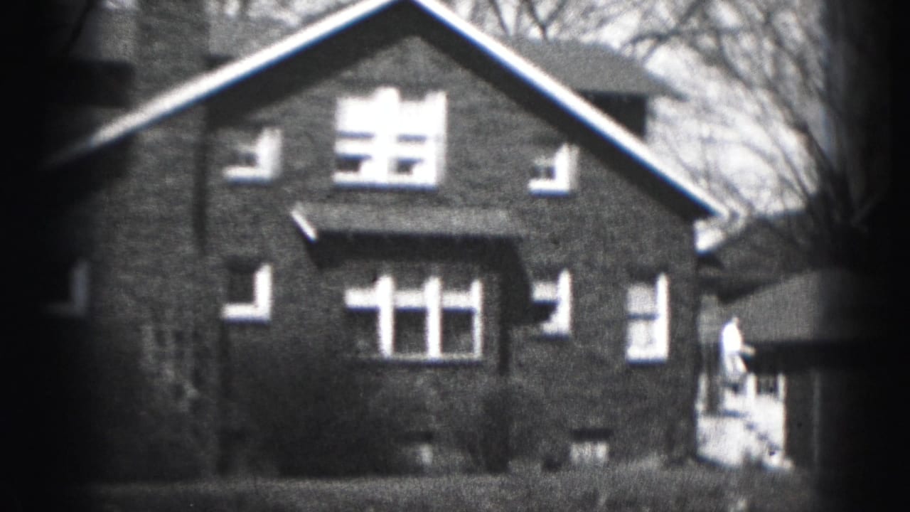 Two-story brick house with gabled roof, chimney, windows, shrubs, and lawn.