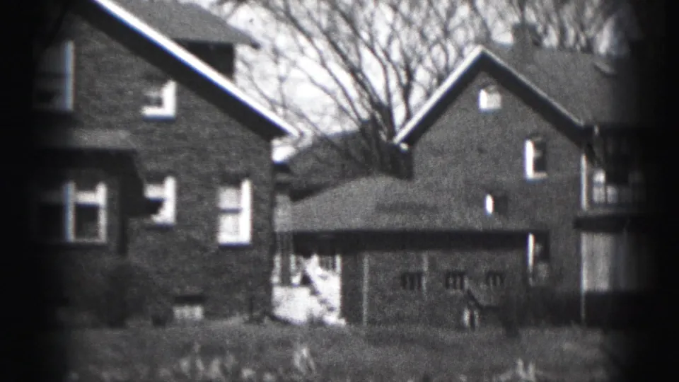 1975 Harrisburg frame with a closer view of adjoining brick houses, garage doors, rooflines, side wall, bare trees, and front lawn.