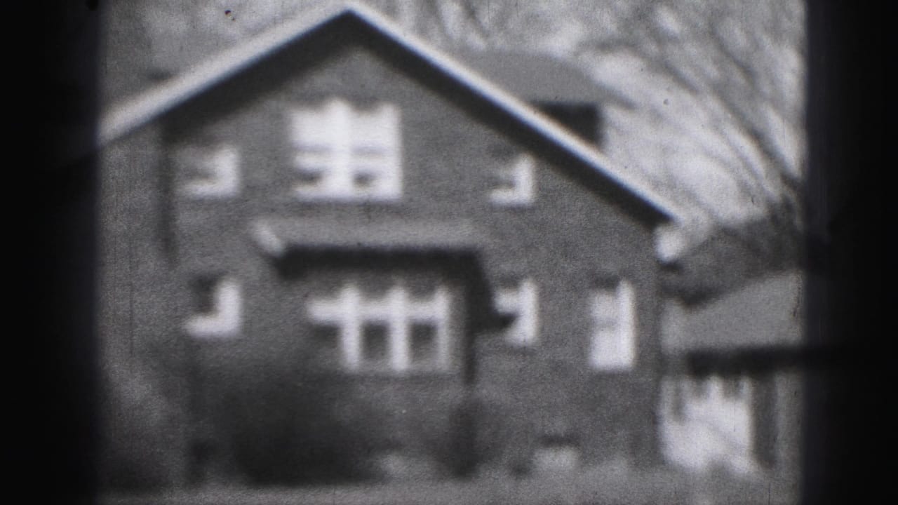 Soft 8mm frame of a brick two-story house with gabled roof, windows, shrubs, and dark frame edges.