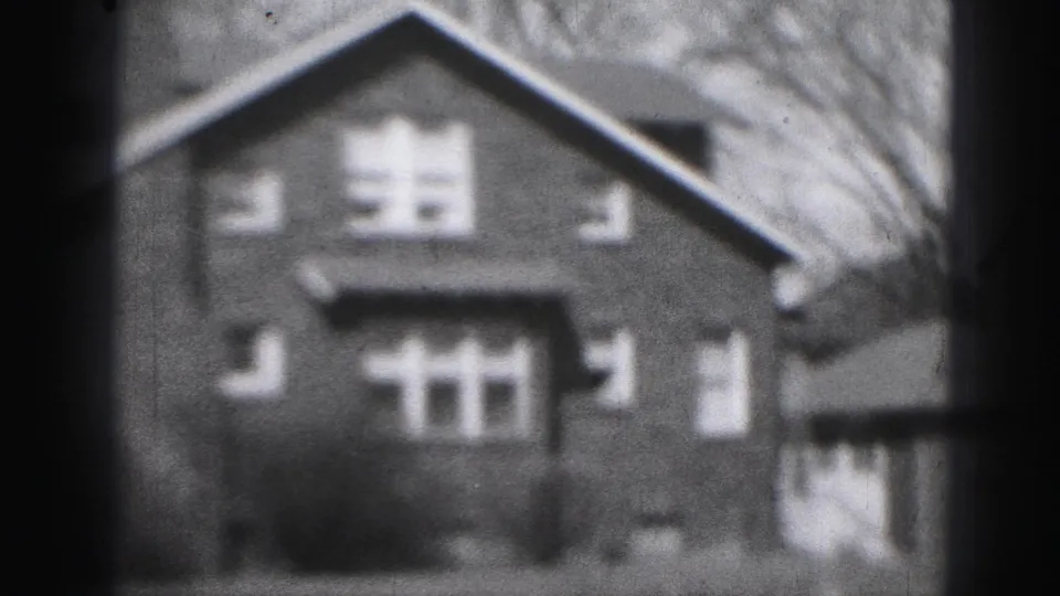 1975 Harrisburg 8mm view of a brick residential house with gabled roof, chimney, windows, shrubs, and lawn in soft focus.